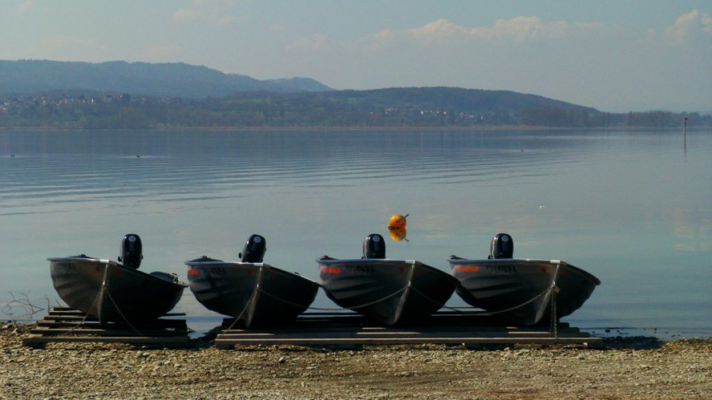 Cuatro pequeñas embarcaciones de alquiler con motor fueraborda, varadas sobre palés en la orilla de un lago