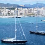 Dos grandes veleros navegan por la bahía de Palma con el puerto deportivo y la ciudad al fondo