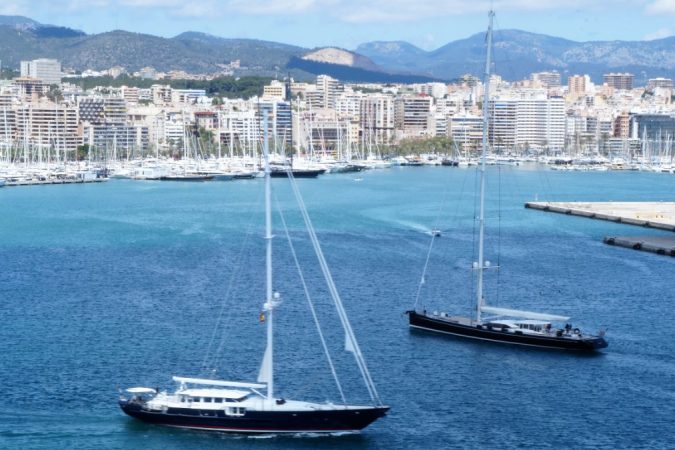 Dos grandes veleros navegan por la bahía de Palma con el puerto deportivo y la ciudad al fondo