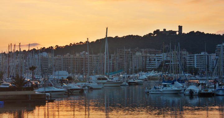 Embarcaciones amarradas en el puerto de Palma al atardecer, con el castillo de Bellver al fondo