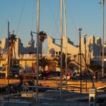Edificio del Centre Municipal de Vela de Barcelona en el Port Olímpic, con embarcaciones y mástiles en primer plano al atardecer