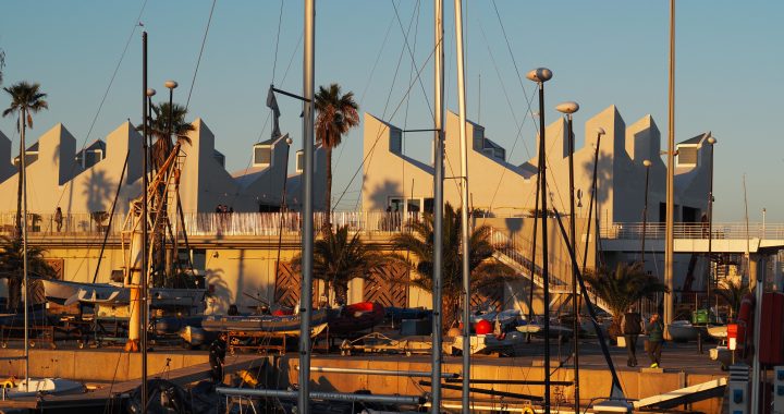 Edificio del Centre Municipal de Vela de Barcelona en el Port Olímpic, con embarcaciones y mástiles en primer plano al atardecer