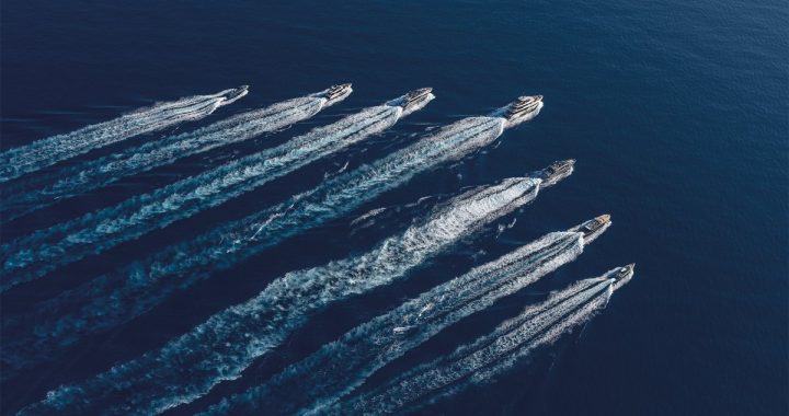 Vista aérea de siete yates a motor navegando en formación sobre el mar, dejando largas estelas blancas