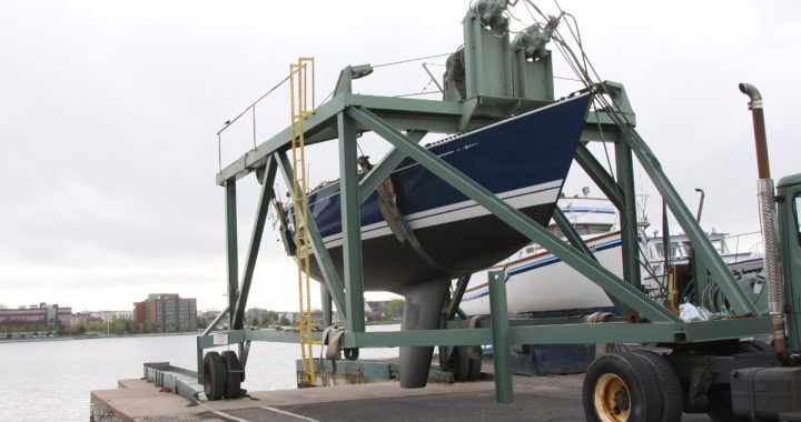 Velero suspendido de una grúa pórtico (travel lift) junto al muelle de un club náutico