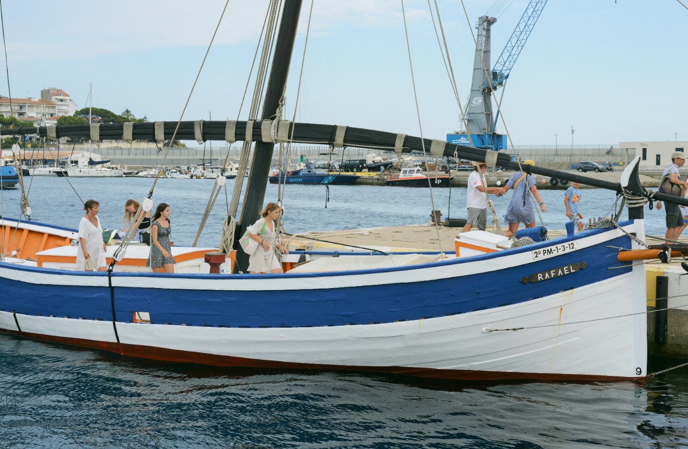 La barca de bou Rafael, de casco blanco y azul, amarrada en el puerto de Palamós con la antena arriada sobre cubierta