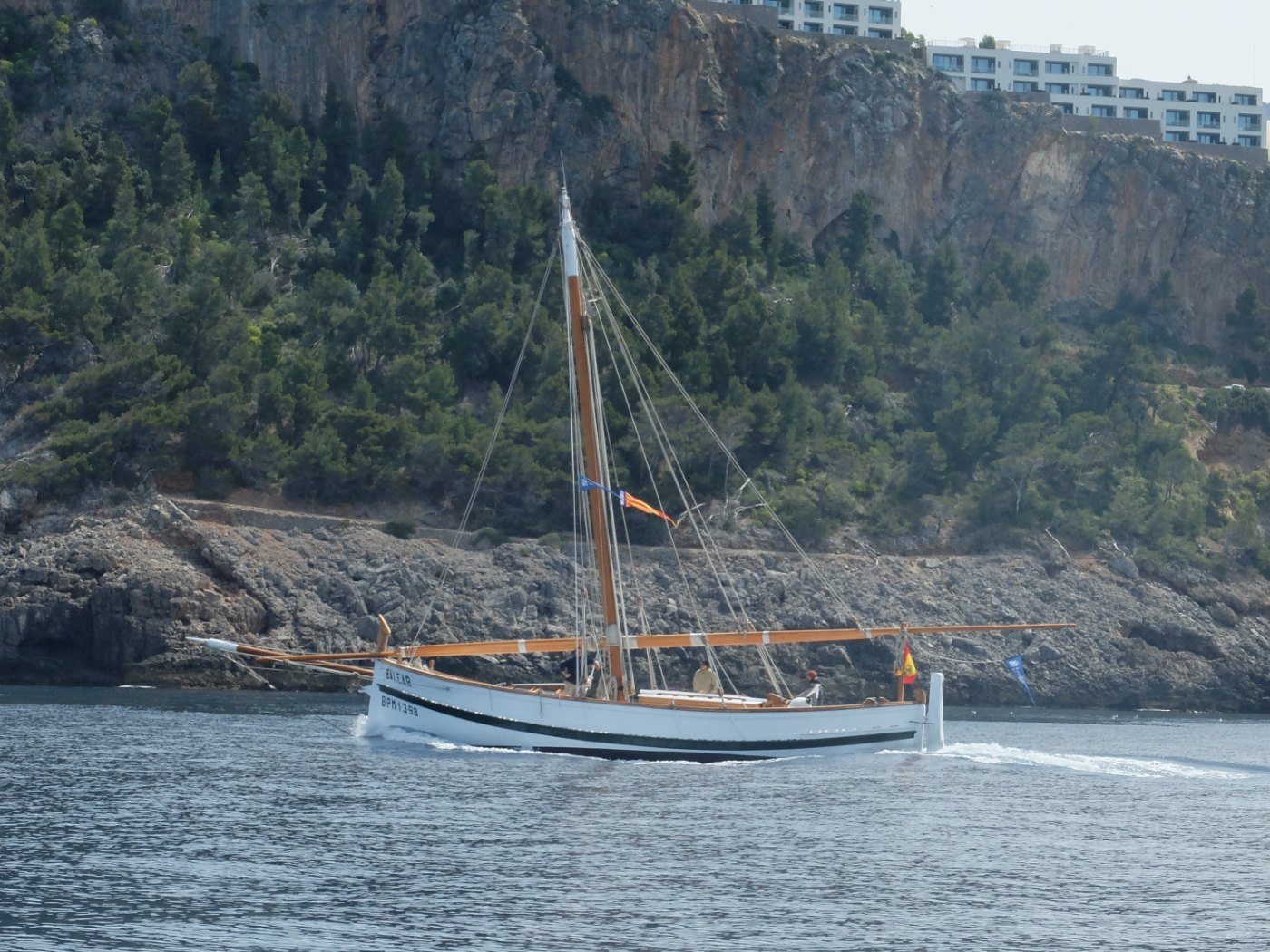 El llaüt Balear, con la antena arriada, navegando junto a los acantilados a la salida del puerto de Sóller