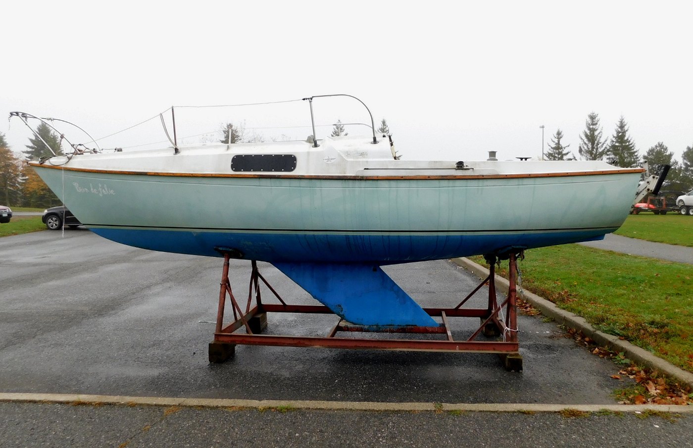 Velero pequeño apoyado en su cuna metálica en tierra, con la obra viva pintada de azul y la quilla a la vista