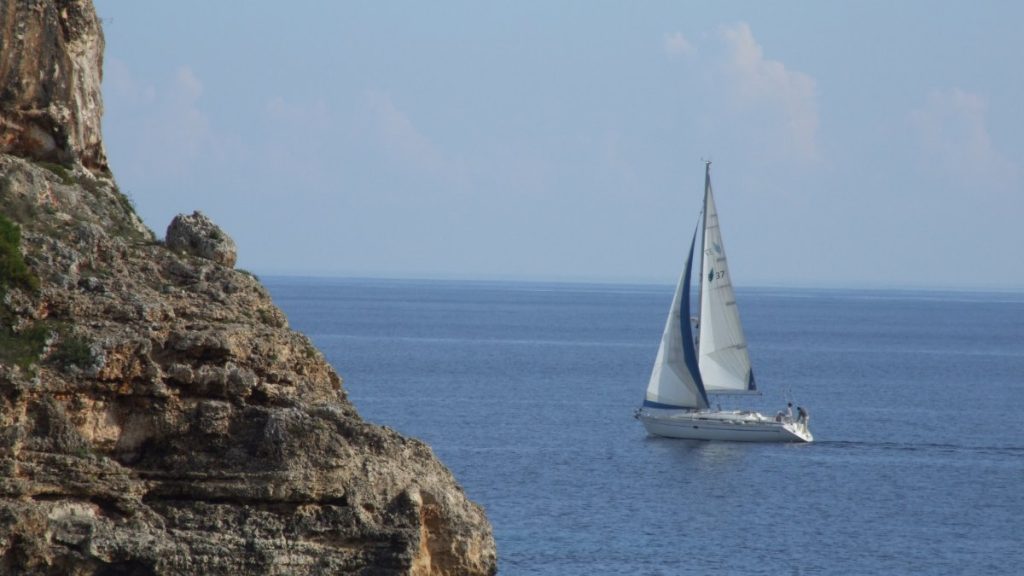 Velero de crucero con la mayor y la vela de proa izadas navegando junto a un acantilado de la costa de Mallorca