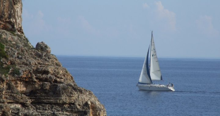 Velero de crucero con la mayor y la vela de proa izadas navegando junto a un acantilado de la costa de Mallorca