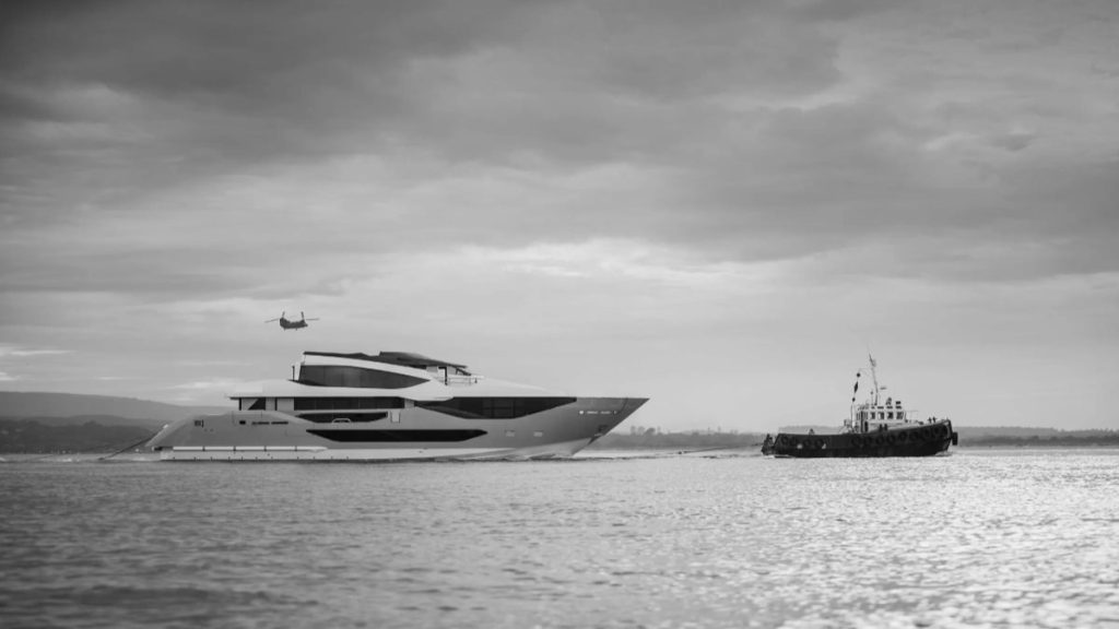 El primer Sunseeker 134 navega remolcado por un remolcador hacia Poole, en una fotografía en blanco y negro con un helicóptero al fondo