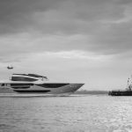 El primer Sunseeker 134 navega remolcado por un remolcador hacia Poole, en una fotografía en blanco y negro con un helicóptero al fondo