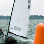Un regatista de la clase Europe navega con viento fresco junto a una boya naranja de regata