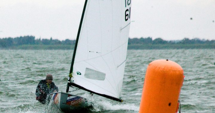Un regatista de la clase Europe navega con viento fresco junto a una boya naranja de regata