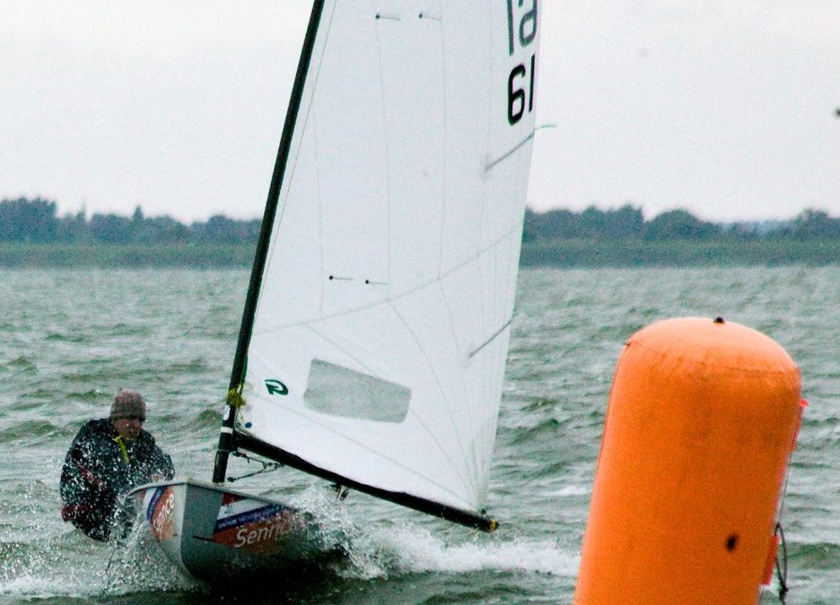 Un regatista de la clase Europe navega con viento fresco junto a una boya naranja de regata